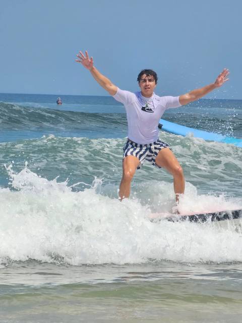 Action shot of a surfer riding a small wave wearing striped shorts and white rash guard