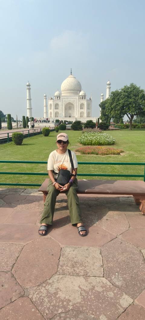 A traveller sits on a bench in a manicured park on a sunny day.