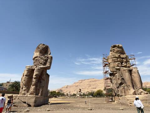 The Colossi of Memnon tower over visitors with desert cliffs in the background.