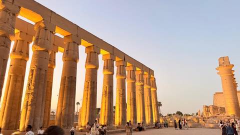 Golden sunset light bathes the colossal columns of Luxor Temple as visitors wander below.