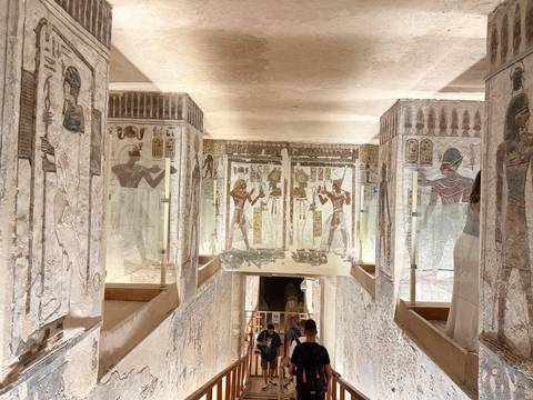 Visitors descend a richly painted corridor inside a pharaonic tomb.