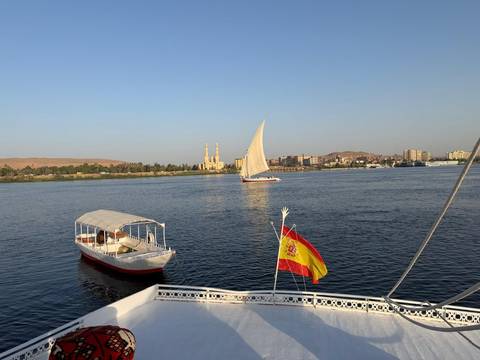 A felucca and motorboat sail on the Nile with Aswan’s riverside skyline beyond.