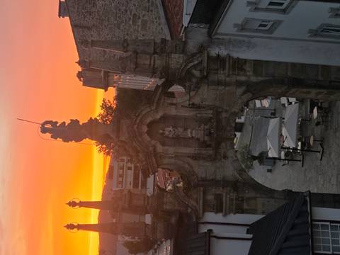 Historic stone archway and statue silhouetted against a vivid orange sunset sky.