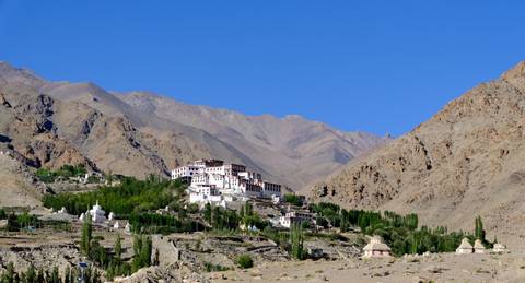 A remote monastery complex surrounded by green poplar trees and arid mountain ranges beneath a cloudless deep-blue sky.