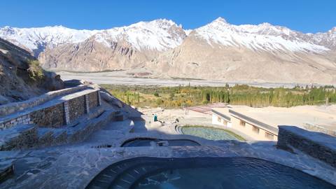 Tiered hillside resort pools and terraces face expansive stony plains and soaring snowy peaks.