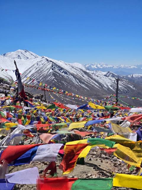 Hundreds of brightly coloured prayer flags fluttering atop a snowy mountain pass with rugged peaks beyond.