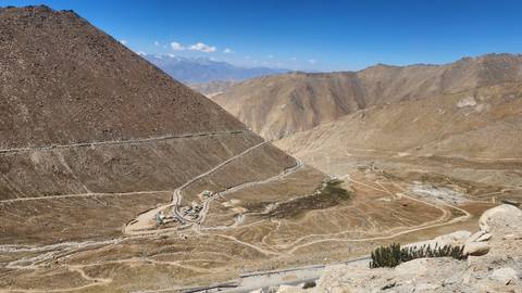 A winding high-altitude road snakes across a barren brown mountain landscape under clear skies.