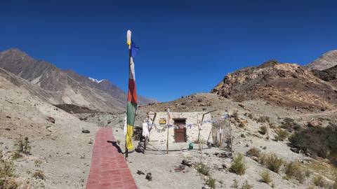A small white shrine adorned with prayer flags stands in a stark rocky desert valley.