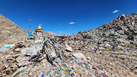 Rocky mountain pass strewn with colourful prayer flags beneath a vivid blue sky.