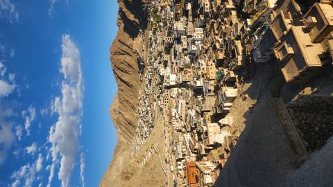 Panoramic view of Leh town sprawled across a valley, captured in warm late-afternoon light with rugged hills around.