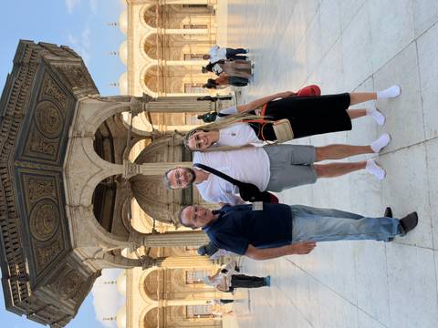 Three visitors stand barefoot posing inside a historic mosque courtyard with ornate fountain.