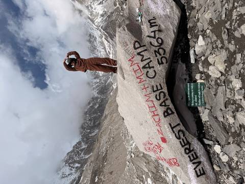 Traveller posing on a boulder marked Everest Base Camp 5364 m amid rugged Himalayan scenery