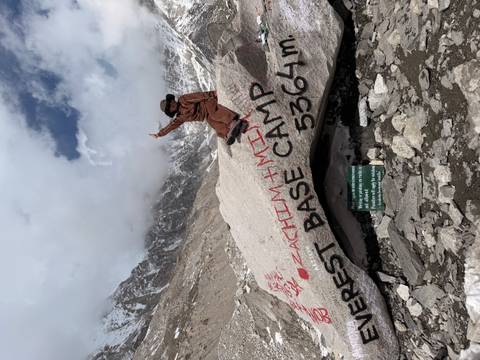 Hiker sitting on the Everest Base Camp boulder raising an arm with snowy peaks behind