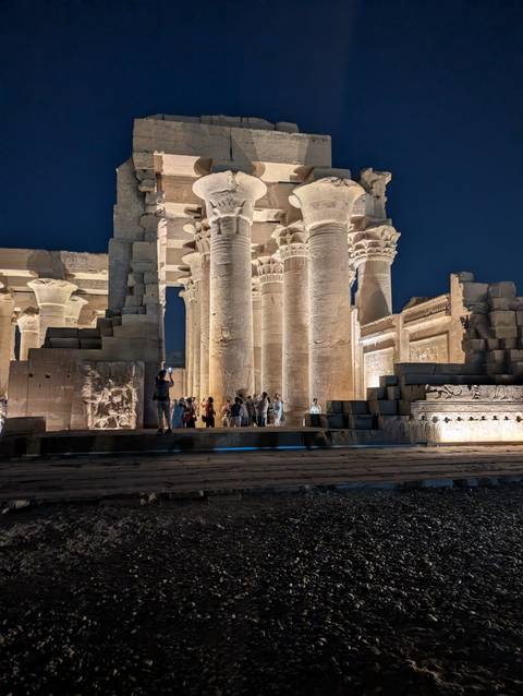 Night illumination of Kom Ombo temple columns with intricate hieroglyphs and tourists below