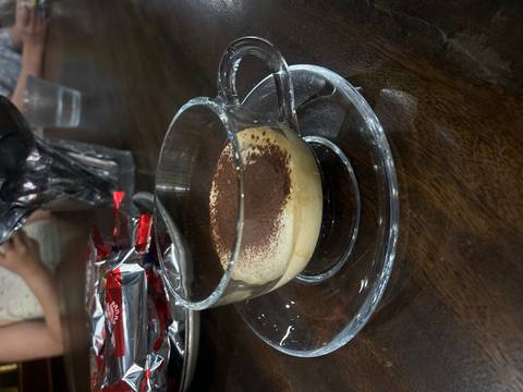 Glass cup of creamy Vietnamese egg coffee dusted with cocoa powder on a saucer