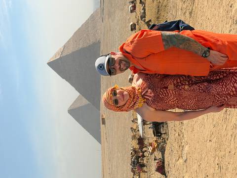 Smiling couple posing in the desert with the Great Pyramids rising behind them under a blue sky.