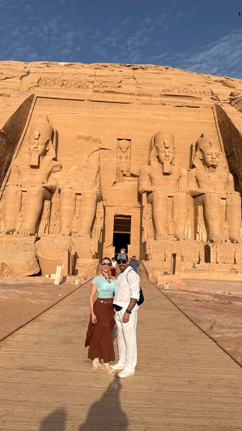 Couple standing before the colossal statues of Abu Simbel temple bathed in warm sunlight.