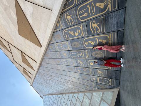 Couple standing against a monumental museum facade covered in giant golden hieroglyph panels.