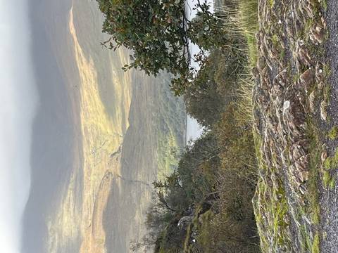 Sun breaks through clouds illuminating a mountainous Irish valley with a distant lake.