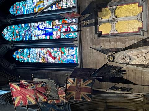 Interior shot of stained glass windows, medieval flags, and stone walls inside a cathedral.
