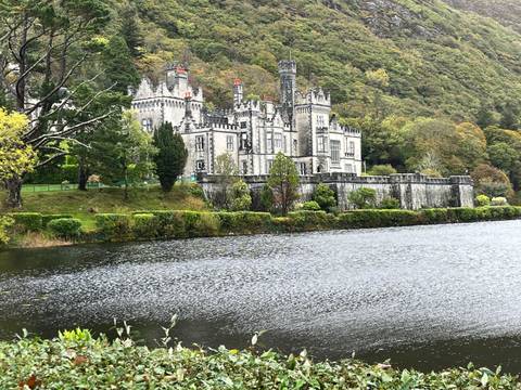 Grand neo-Gothic Kylemore Abbey reflected in a lake amid lush wooded hillside.
