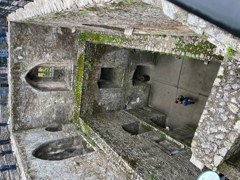 Top-down view into the stone interior chambers of Blarney Castle with two visitors below.