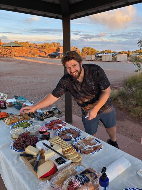 Traveler arranging picnic foods on a table at a desert campsite during golden hour.