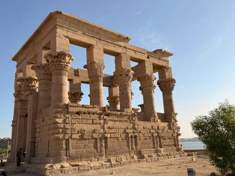 Sandstone kiosk with ornate columns at Philae Temple glowing in warm light beside the Nile River.