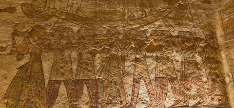 Warmly lit close-up of ancient Egyptian relief carvings depicting a ceremonial procession on a stone wall.