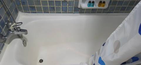 White bathtub with shower curtain and small toiletry bottles against mosaic tiles.