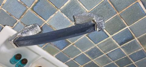 Close-up of a broken plastic grab bar on a tiled bathroom wall with toiletries nearby.