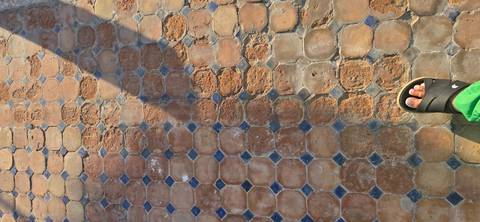 Ground-level view of patterned pavement with a sandal-clad foot and long shadow.