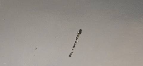Close-up of a grey wall with a long scratch exposing underlying material.