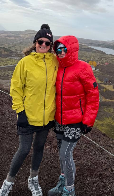 Two travellers in colourful jackets pose together on a rocky volcanic slope.