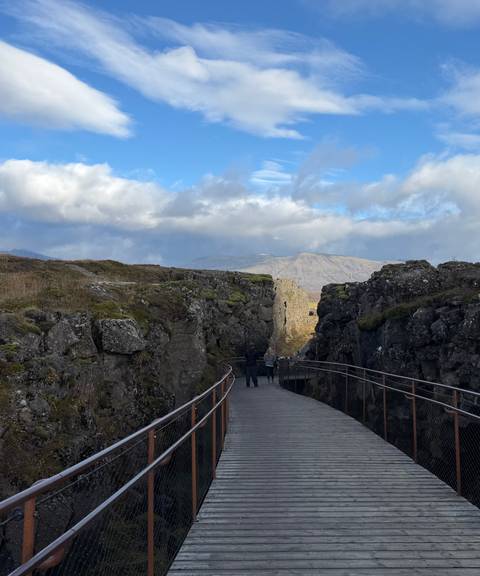 Boardwalk threads through dramatic rocky rift walls towards distant mountains under a bright sky.