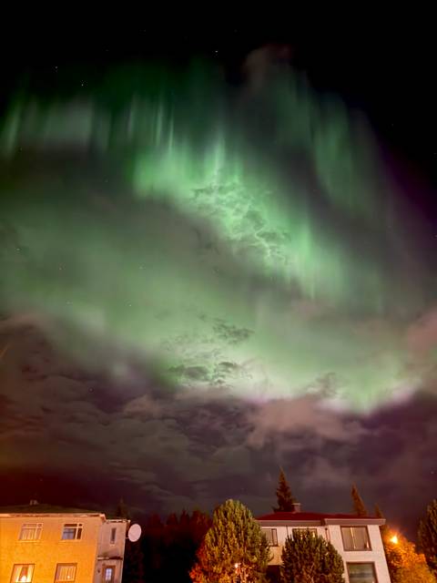 Vibrant green aurora borealis curtains dance across a starry night sky.