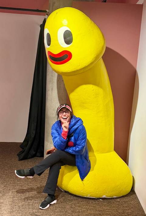 Visitor laughs while posing beside a giant yellow sculpture inside a quirky museum.