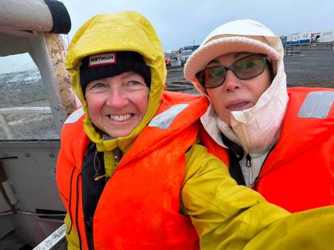 Selfie of two women in bright orange life vests on a grey day at a harbour.