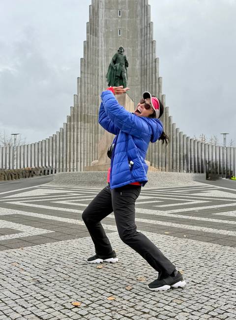Energetic traveller pretends to hold up Hallgrimskirkja church while standing on patterned pavement.