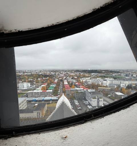 View through a window frame shows Reykjavik’s colourful rooftops spreading beneath a grey sky.