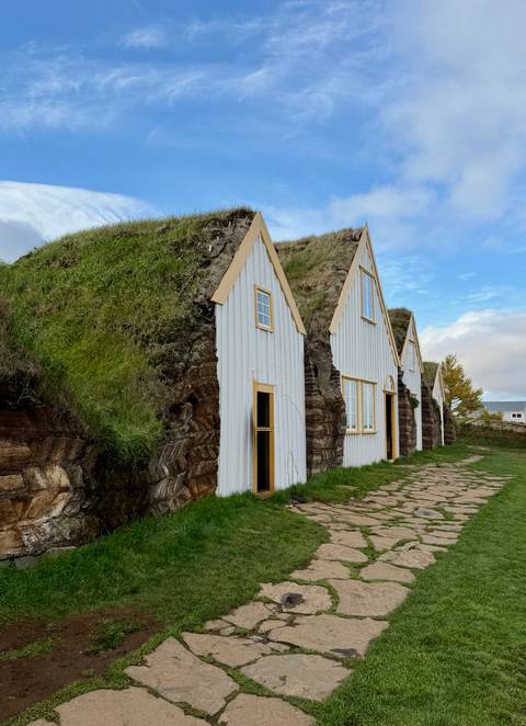 Traditional turf-roofed white timber houses nestle into grassy earth banks beneath a bright sky.