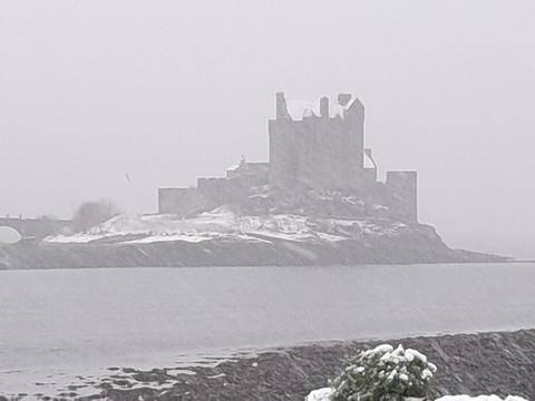 Silhouetted castle on an islet barely visible through heavy snowfall and grey mist across a cold loch.