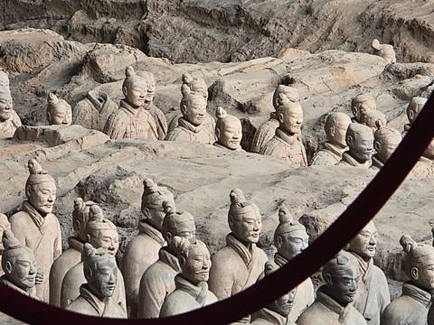 Rows of excavated Terracotta Warrior figures partially buried in earthen pits.