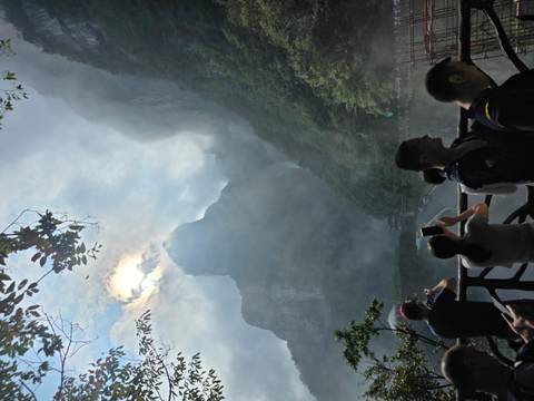 Tourists photograph mist-shrouded quartz sandstone peaks of Zhangjiajie rising dramatically into the clouds.