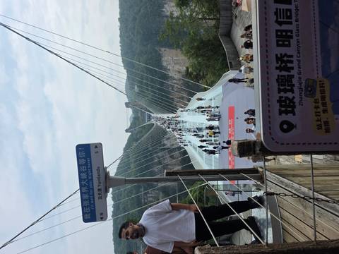 Crowds walk across the glass-bottom Zhangjiajie Grand Canyon Bridge suspended high above a forested gorge.