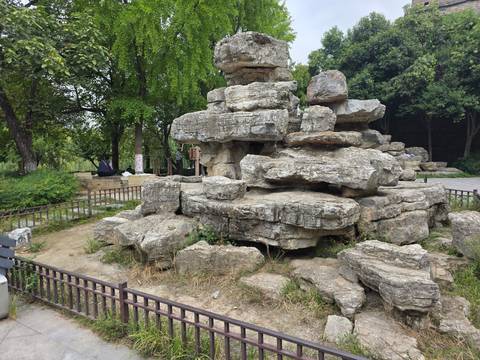Cluster of weathered limestone rocks arranged in a public park area with sparse grass and trees.