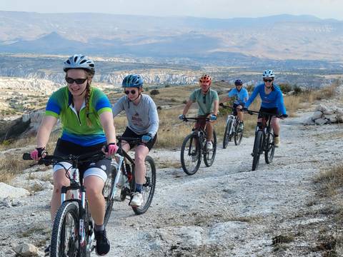 Row of cyclists pedalling up a gravel trail with sweeping views over Cappadocia’s eroded valleys.