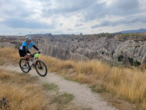 Cyclist rides along a grassy cliff edge overlooking Cappadocia’s wavy ridges of eroded tufa.