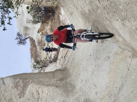 Two cyclists negotiate narrow white-stone gullies, one riding down a steep natural chute.