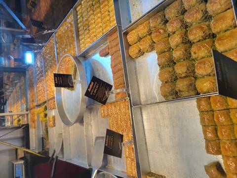 Display trays of freshly baked Turkish baklava varieties glistening with syrup in a pastry shop.